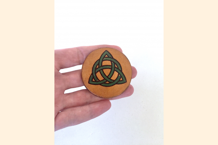 Green Triquetra Magnet held palm side with three fingers to show scale